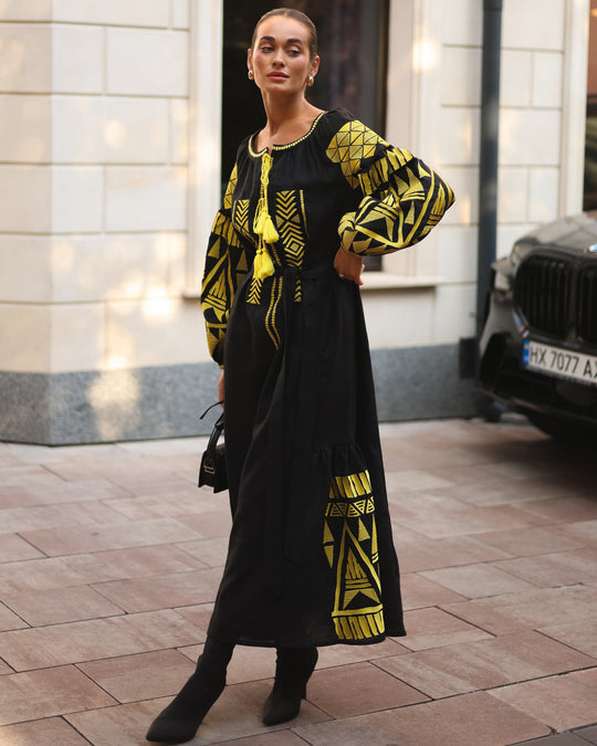 Black linen kaftan maxi dress with gold geometric embroidery, balloon sleeves and gold tassel ties, styled on city street, lifestyle view - Zalxndra Resort