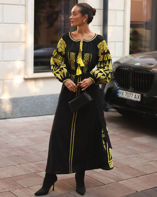Black linen kaftan maxi dress with gold geometric embroidery, balloon sleeves and gold tassel ties, styled with black clutch and boots, full length view - Zalxndra Resort