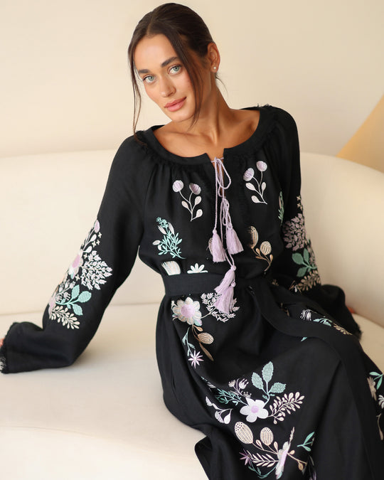 Seated view of black linen kaftan maxi dress with pastel floral embroidery and lilac tassel ties - Zalxndra Resort