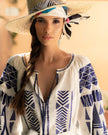 White linen kaftan maxi dress with blue geometric embroidery and balloon sleeves, styled with patterned straw hat, portrait view - Zalxndra Resort
