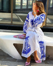 White linen kaftan maxi dress with blue geometric embroidery, balloon sleeves and self-tie belt, seated lifestyle view - Zalxndra Resort