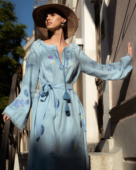 Model styled in powder blue linen kaftan maxi dress with floral embroidery, angel sleeves, and tassel ties on Mediterranean street - Zalxndra Resort