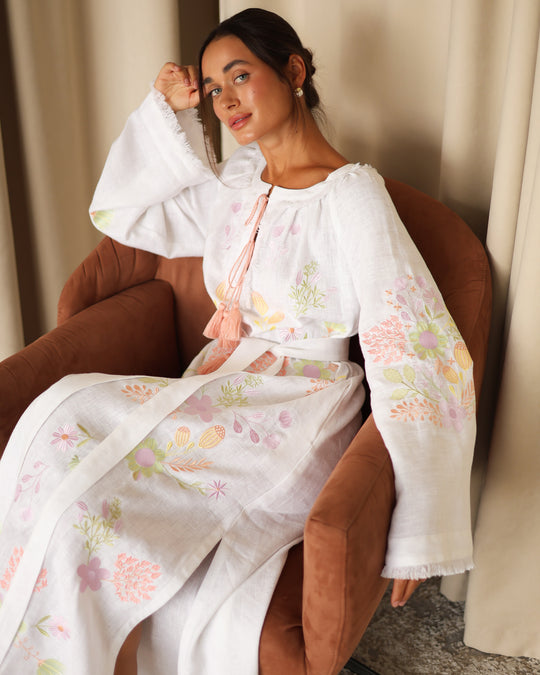 Editorial seated portrait of model in white pastel floral embroidered linen kaftan maxi dress — Zalxndra Resort